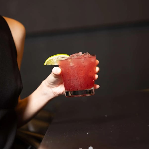 A person in a black top holds a red cocktail with ice and a lime wedge.