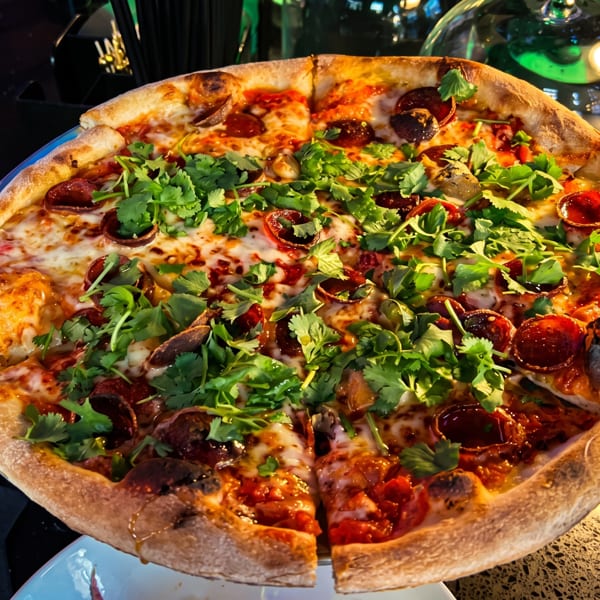 A whole pepperoni pizza topped with fresh cilantro, sliced into eight pieces on a dark table.