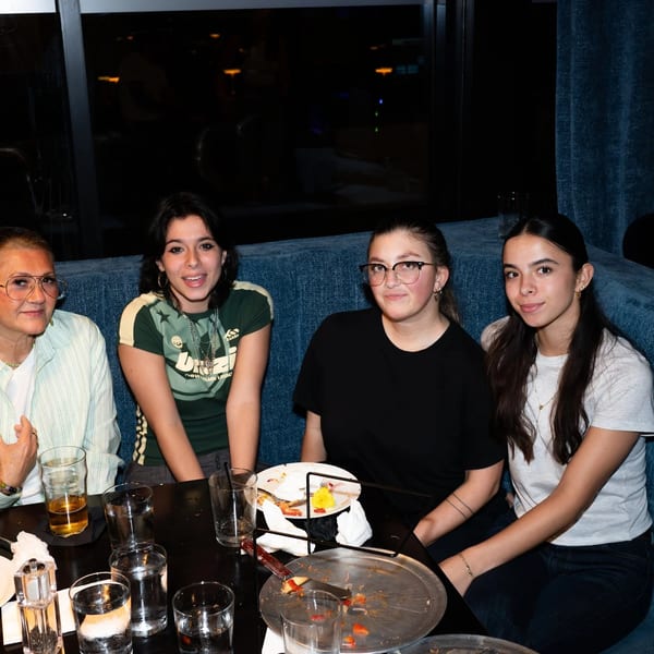 Four women sitting at a dark table with drinks and empty plates in a restaurant.