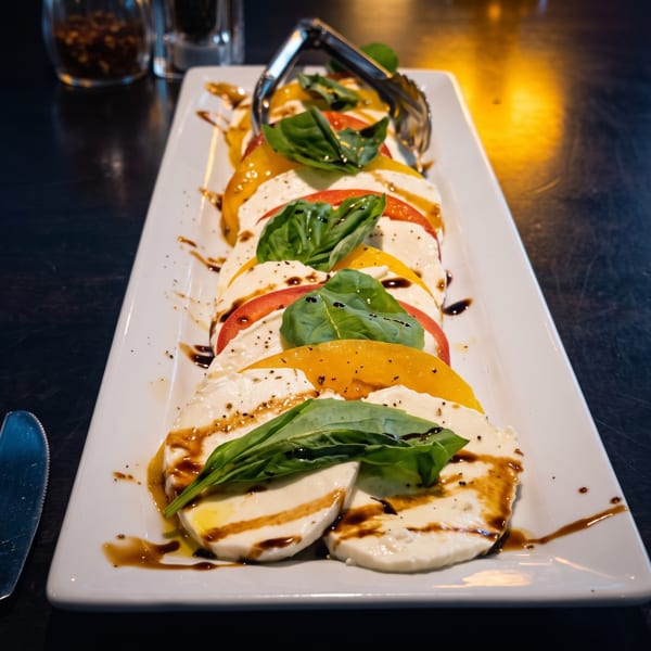Caprese salad with alternating slices of mozzarella, red and yellow tomatoes, basil, and balsamic glaze.