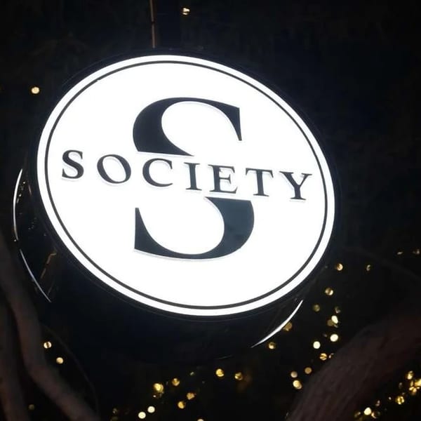 Illuminated circular sign for "SOCIETY" restaurant with a large 'S' in the center, at night.