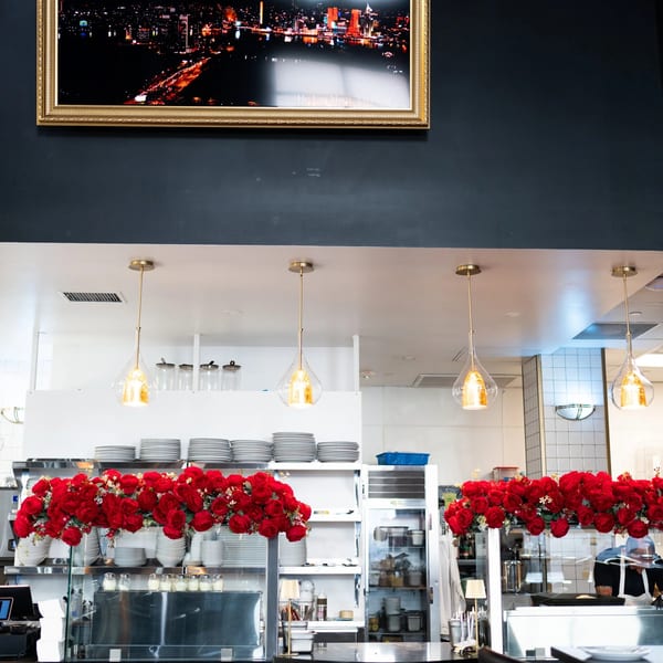 A restaurant interior with a framed cityscape above a counter adorned with red roses and pendant lights.