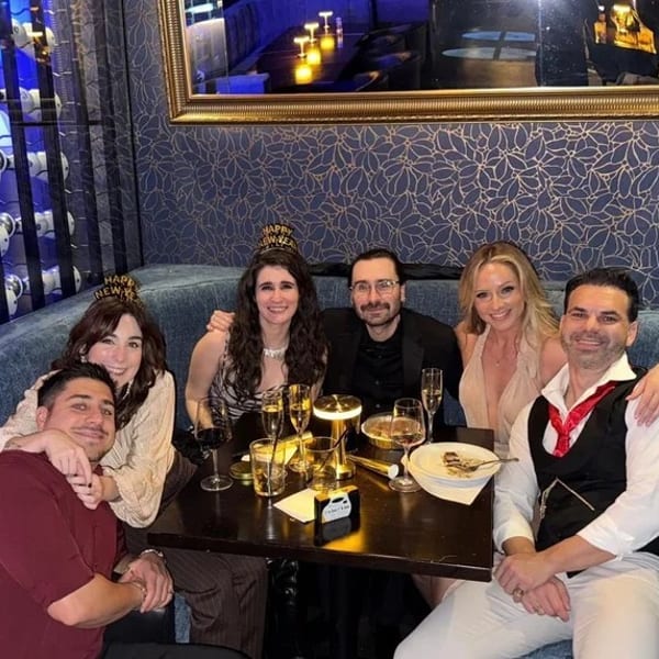 Six friends celebrating New Year's Eve at a restaurant, seated at a table with drinks.
